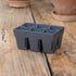 Gray plastic seedling tray on a wooden surface with terracotta pots in the background